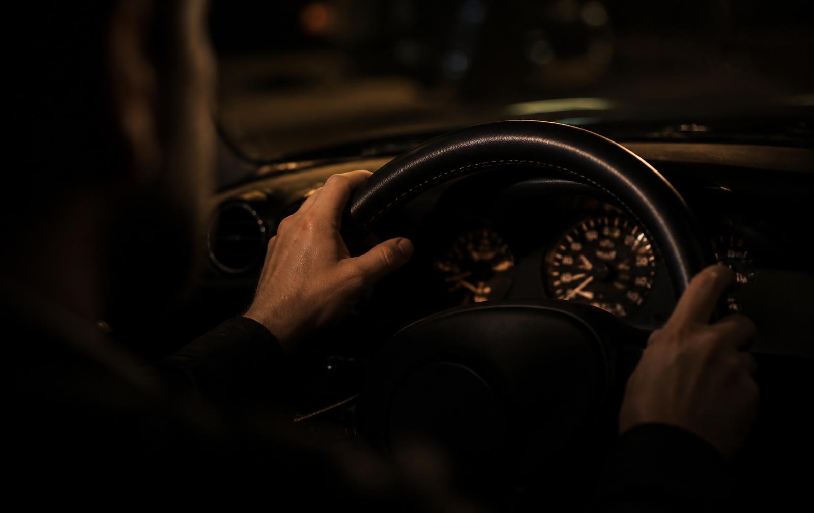 Handen aan het stuur van een luxe auto in de avond